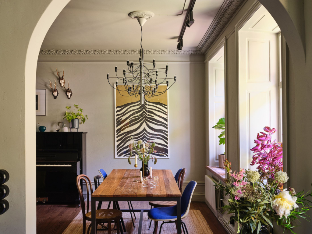 Eclectic maximalism dining room with black chandelier, wooden table, and zebra-patterned wall hanging
